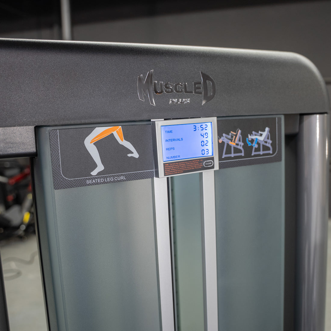 Close-up of a "Muscled Plus" seated leg curl machine with a digital display showing workout stats.