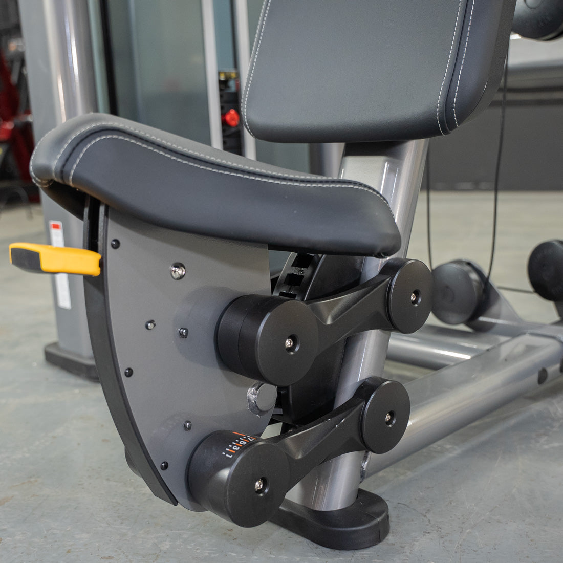 Close-up of the black padded seat and adjustment levers on a gray shoulder press machine.