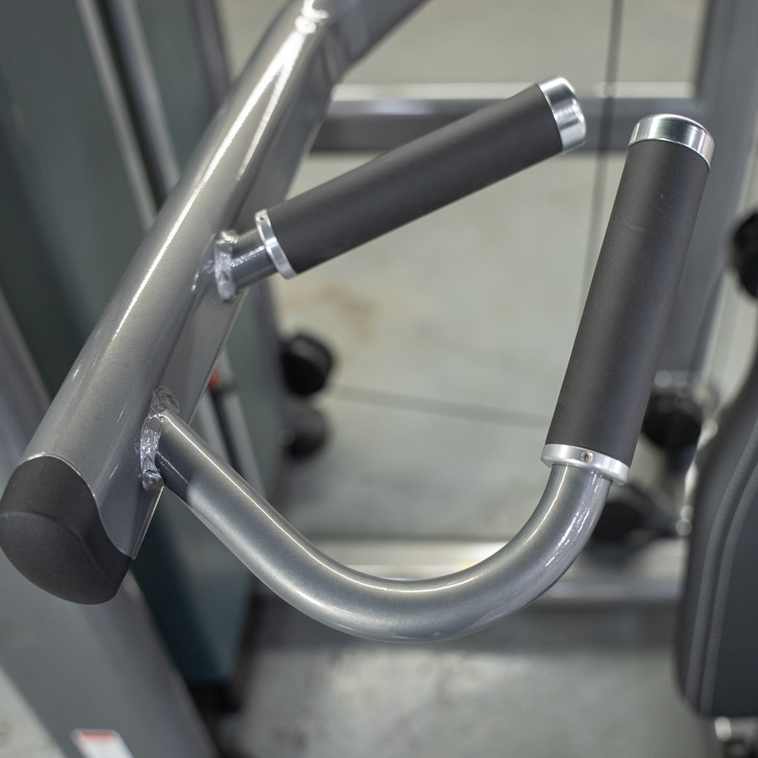 Close-up of the black padded handles and silver frame of the Elite Plus Shoulder Press machine.