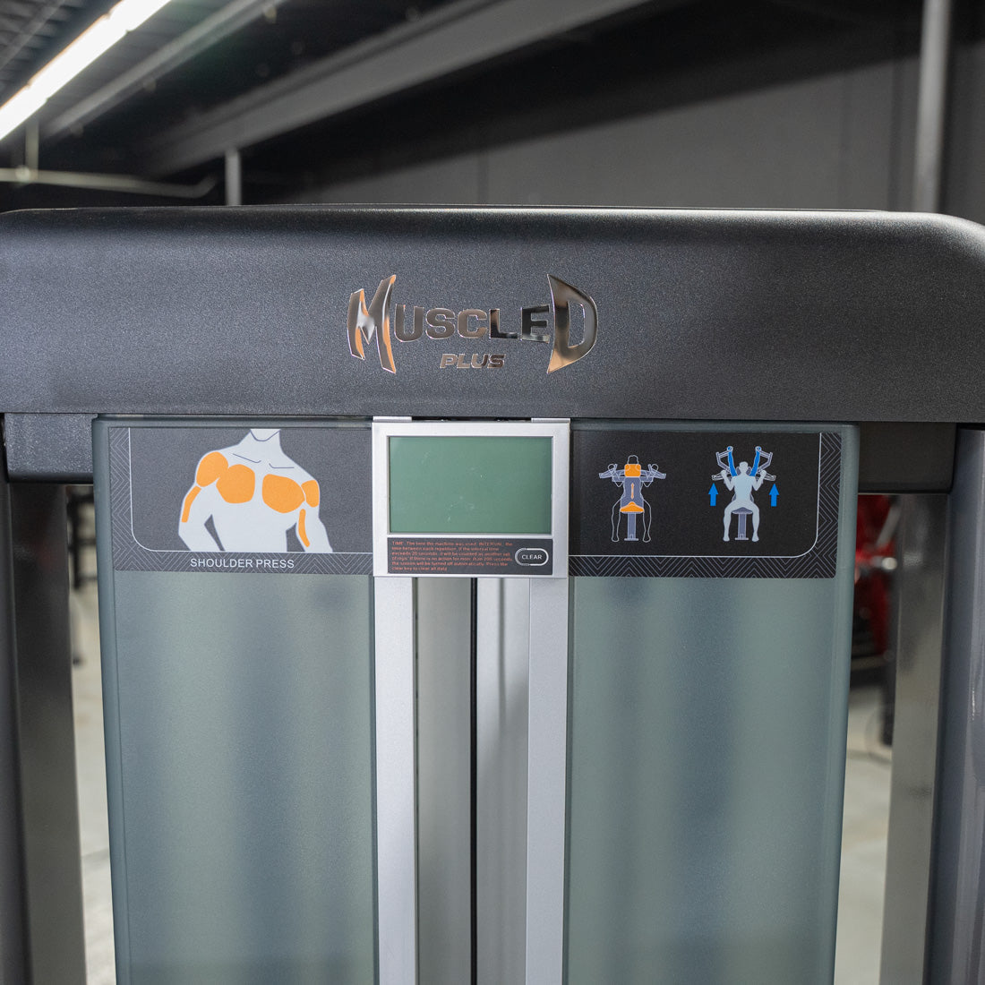 Close-up of Muscle D Plus shoulder press machine with exercise diagrams and digital display.