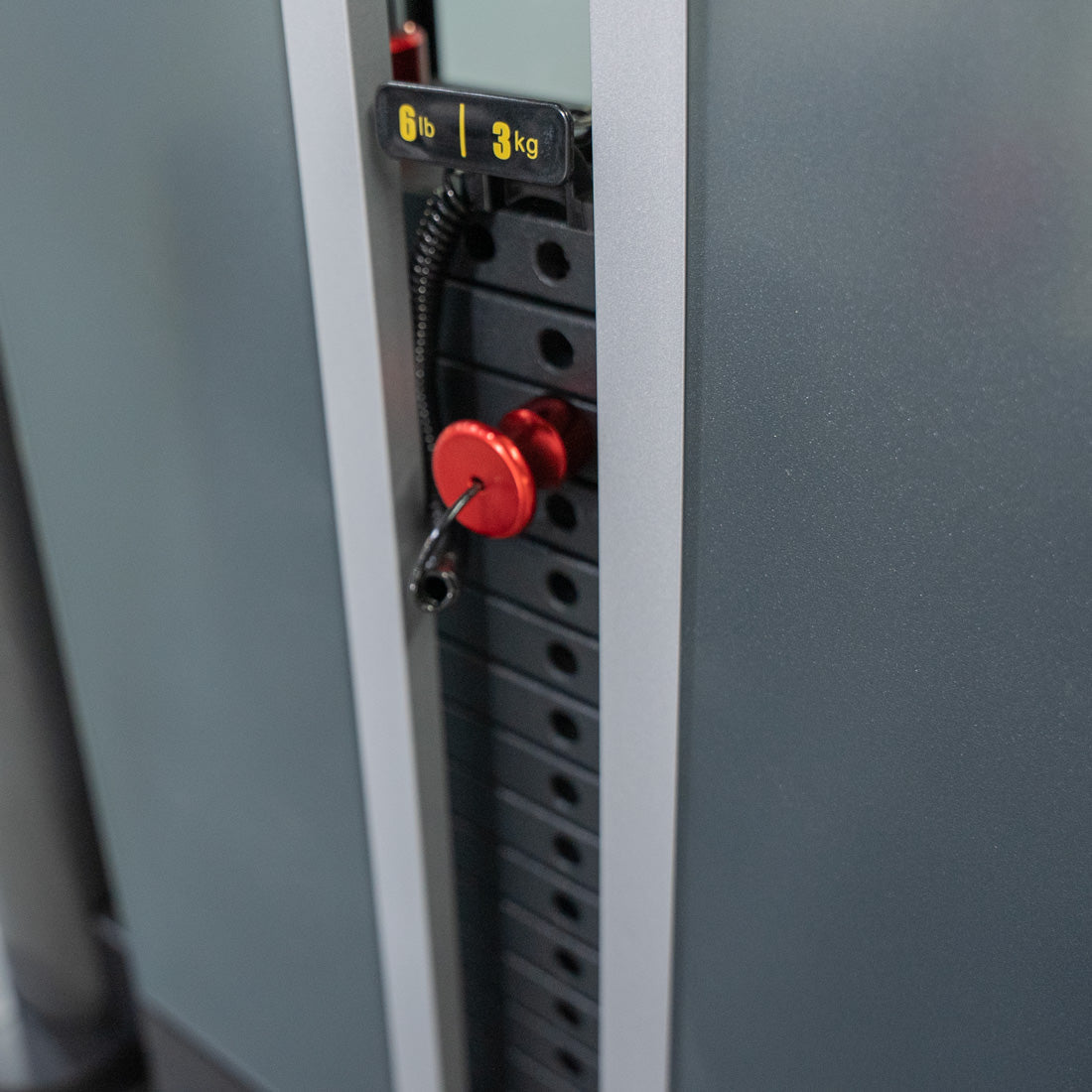 Close-up of gym equipment weight stack with red selector pin and 6lb/3kg increment plate.