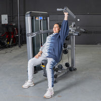 Thumbnail for Woman in tie-dye hoodie using a shoulder press machine in a gym.