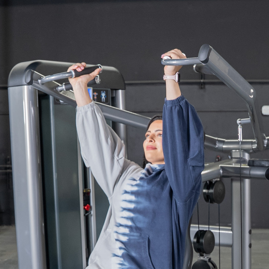 Woman using a shoulder press machine, holding handles with arms extended upwards.