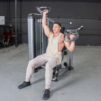 Thumbnail for Man using a shoulder press machine, pushing one handle up and holding the other at shoulder height.