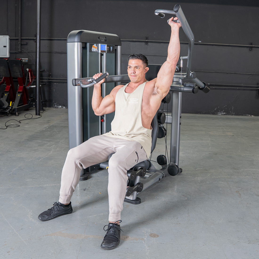 Man in a gym using a shoulder press machine, one arm extended upwards.