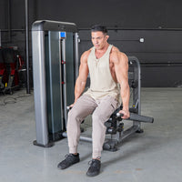 Thumbnail for Man in a tank top using an Elite Plus Triceps Press Machine in a gym.