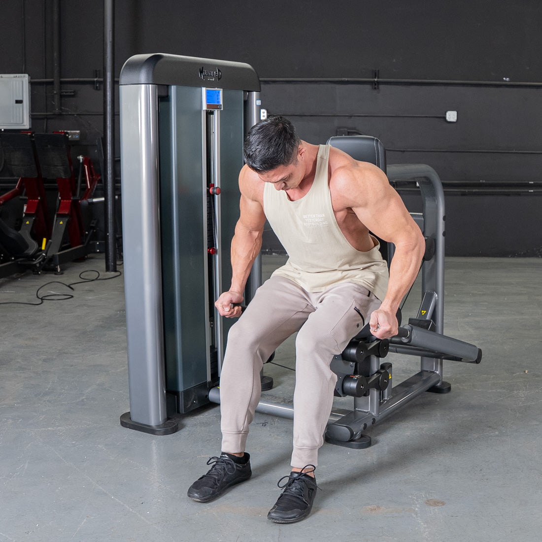 Man in a tank top and sweatpants using a triceps press machine in a gym.
