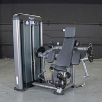 Thumbnail for Gray and black biceps curl machine with padded seat and armrests in a gym.
