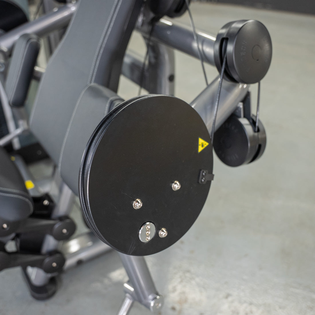 Close-up of a biceps curl machine with black padding, pulleys, and a warning label.