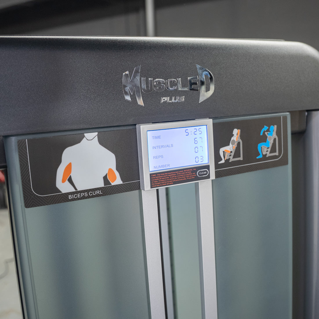 Close-up of a Muscle D Plus biceps curl machine with a digital display showing time, intervals, and reps.