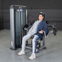 Thumbnail for Woman in tie-dye sweatsuit using a gray biceps curl machine in a gym.