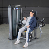 Thumbnail for Woman in tie-dye hoodie using a gray and black biceps curl machine in a gym.