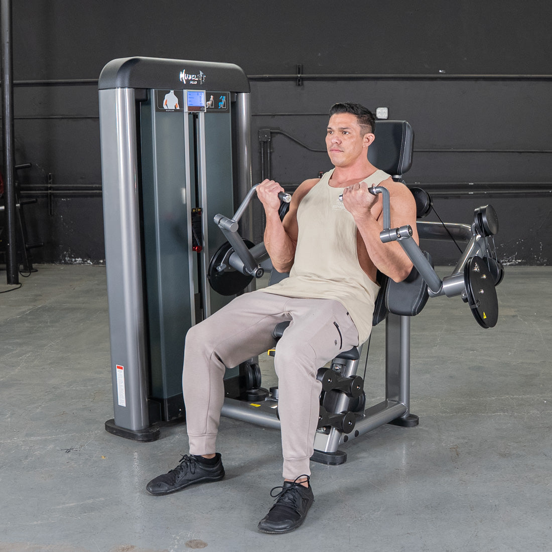 Man in a tank top and sweatpants performing bicep curls on a gray weight machine in a gym.