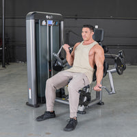 Thumbnail for Man in a tan tank top and gray pants using a gray biceps curl machine in a gym.