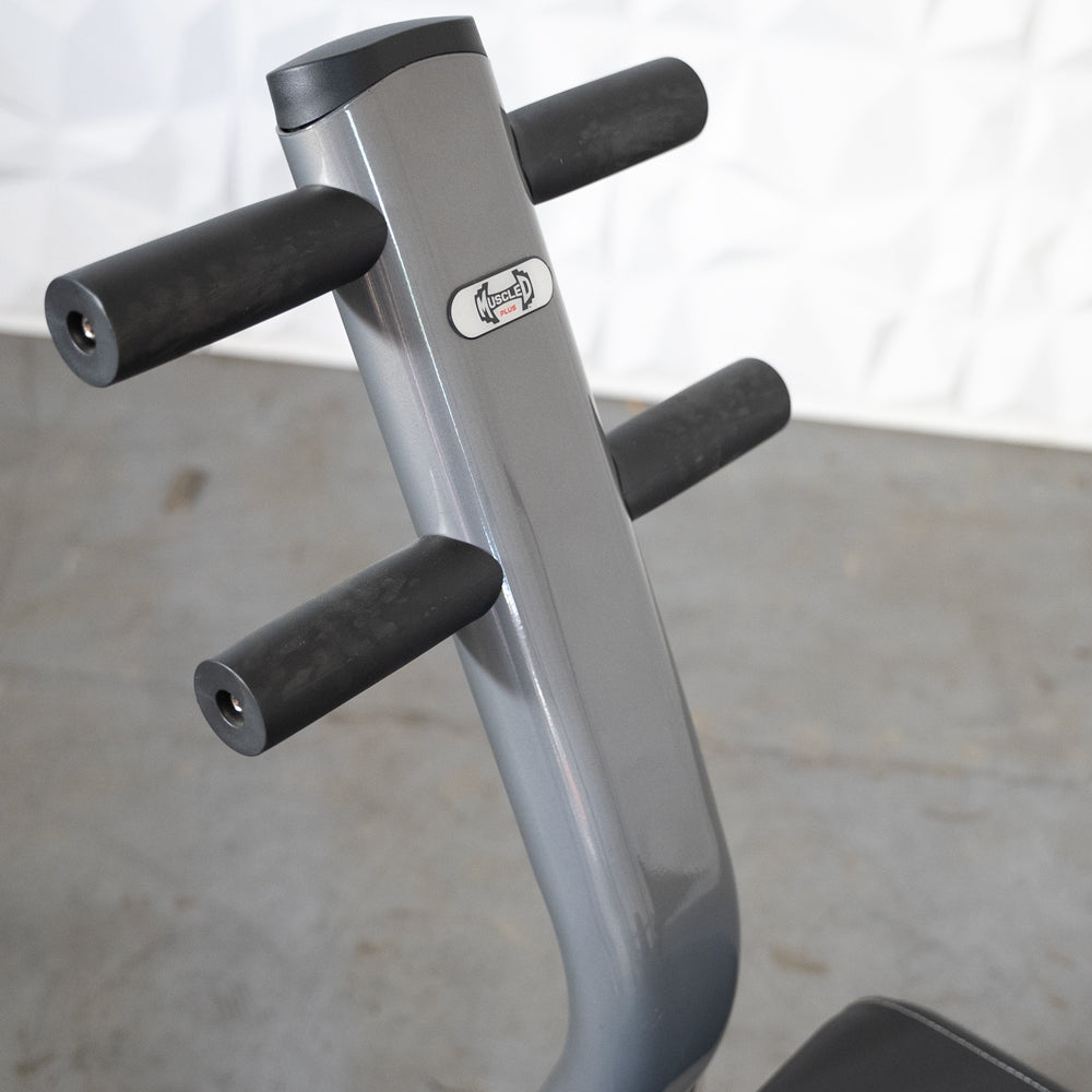 Close-up of the gray frame and black handles of an ab roller, with a "Muscle Plus" logo.