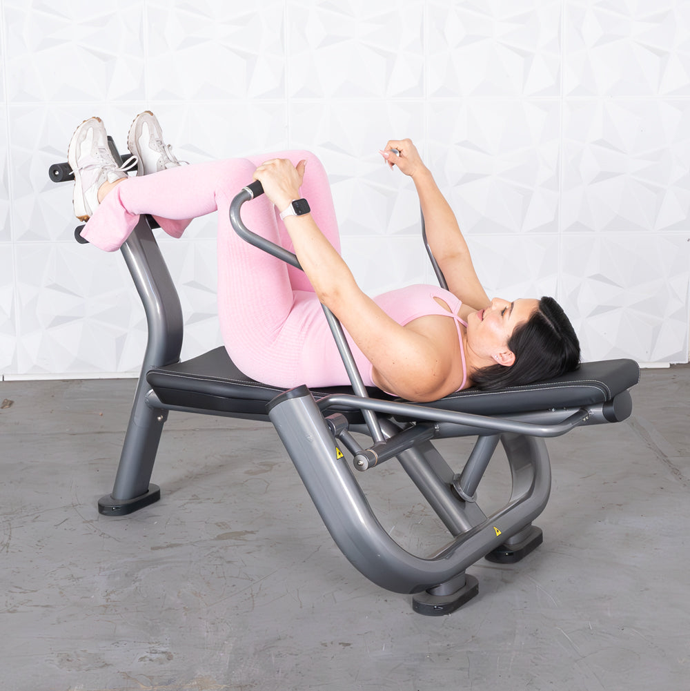 Woman in pink activewear using an ab roller machine, lying on her back with legs raised.