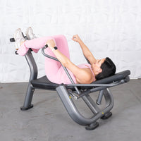 Thumbnail for Woman in pink activewear using an ab roller machine, lying on her back with legs bent and feet secured.