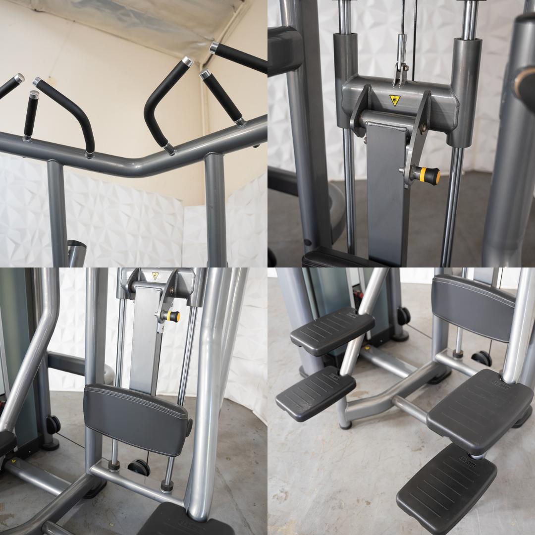 Close-up of a gray assisted chin/dip machine with black handles, seat, and foot platforms.