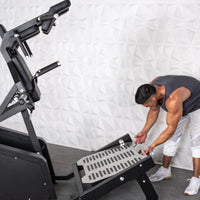 Thumbnail for Man adjusting the footplate on a black plate-loaded squat machine.