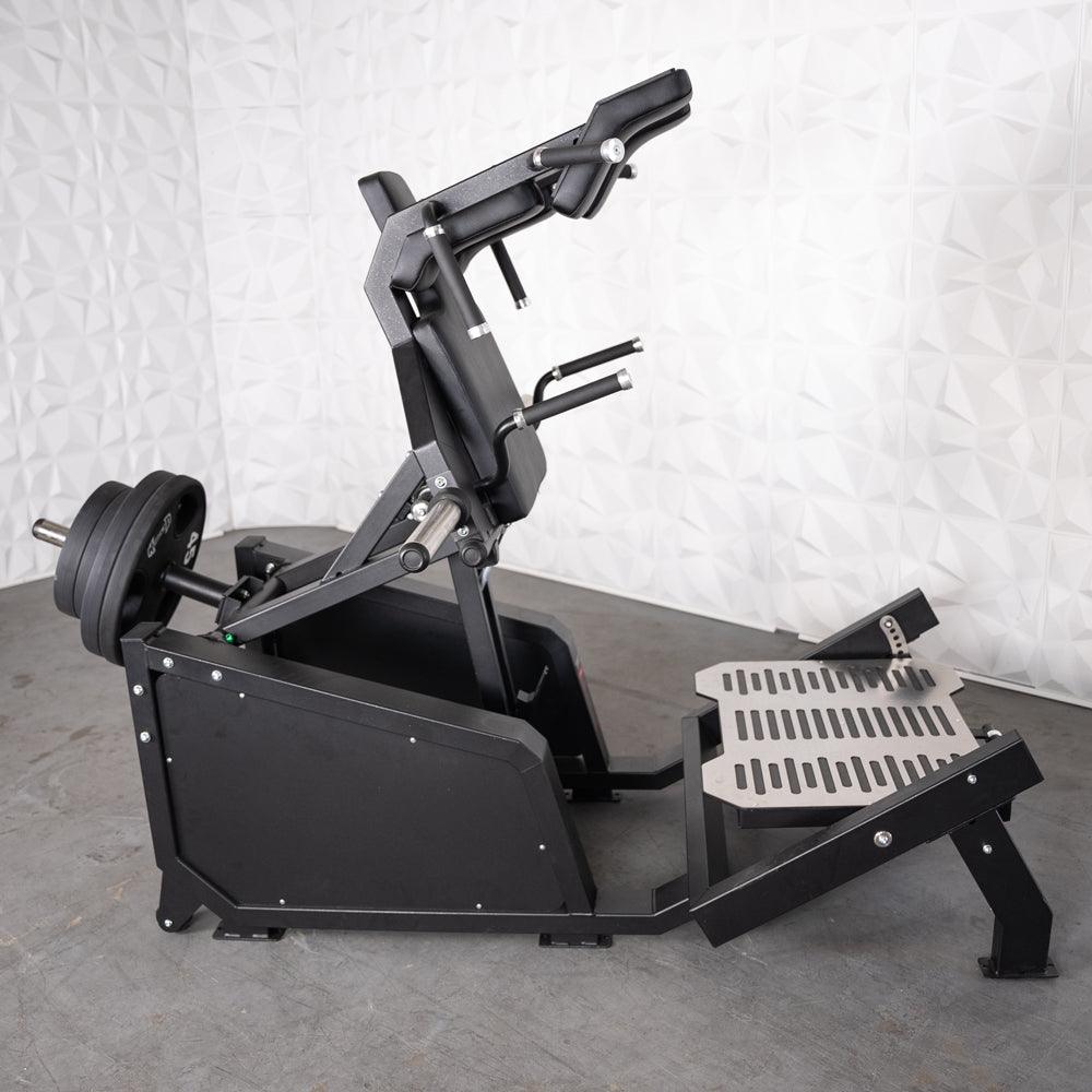 Black plate-loaded hack squat machine with shoulder pads, handles, and foot platform.