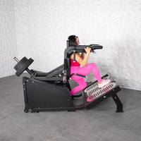 Thumbnail for Woman in pink using a black plate-loaded hack squat machine with weights.