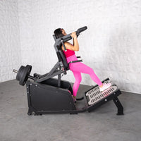 Thumbnail for Woman in pink using a black plate-loaded hack squat machine with weights on the back.