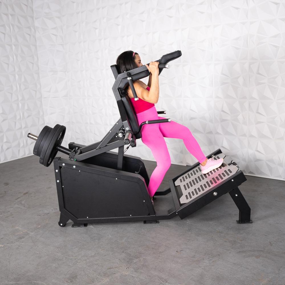 Woman in pink using a black plate-loaded hack squat machine with weights.
