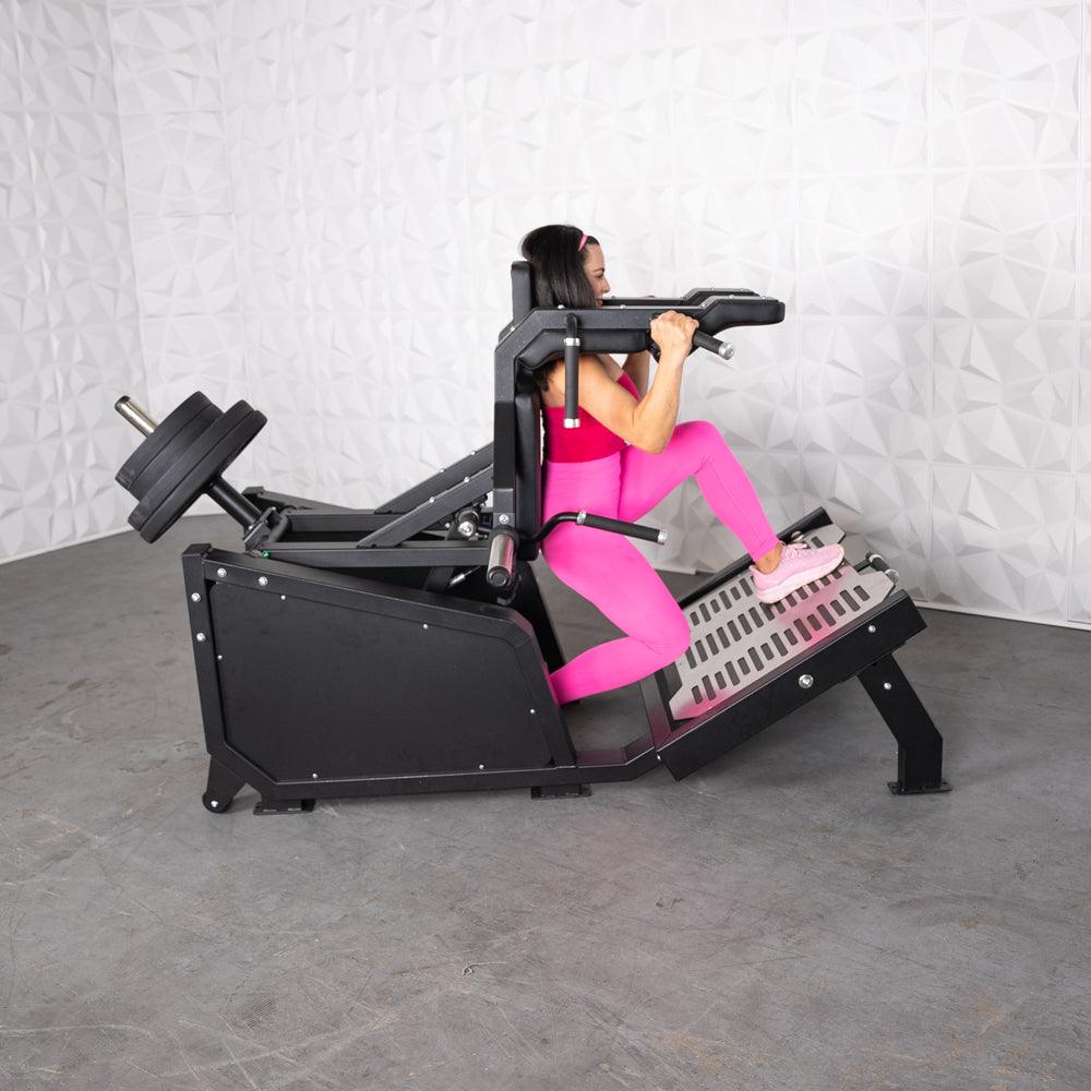 Woman in pink using a black plate-loaded squat machine with weights.