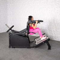 Thumbnail for Woman in pink using a black plate-loaded hack squat machine.