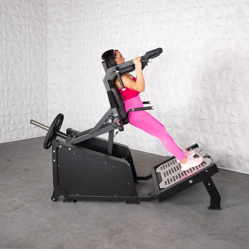 Woman in pink performing a squat on a black plate-loaded hack squat machine.