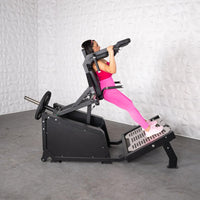 Thumbnail for Woman in pink performing a squat on a black plate-loaded hack squat machine.