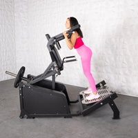 Thumbnail for Woman in pink using a black plate-loaded squat machine with a counter-balanced shoulder pad.