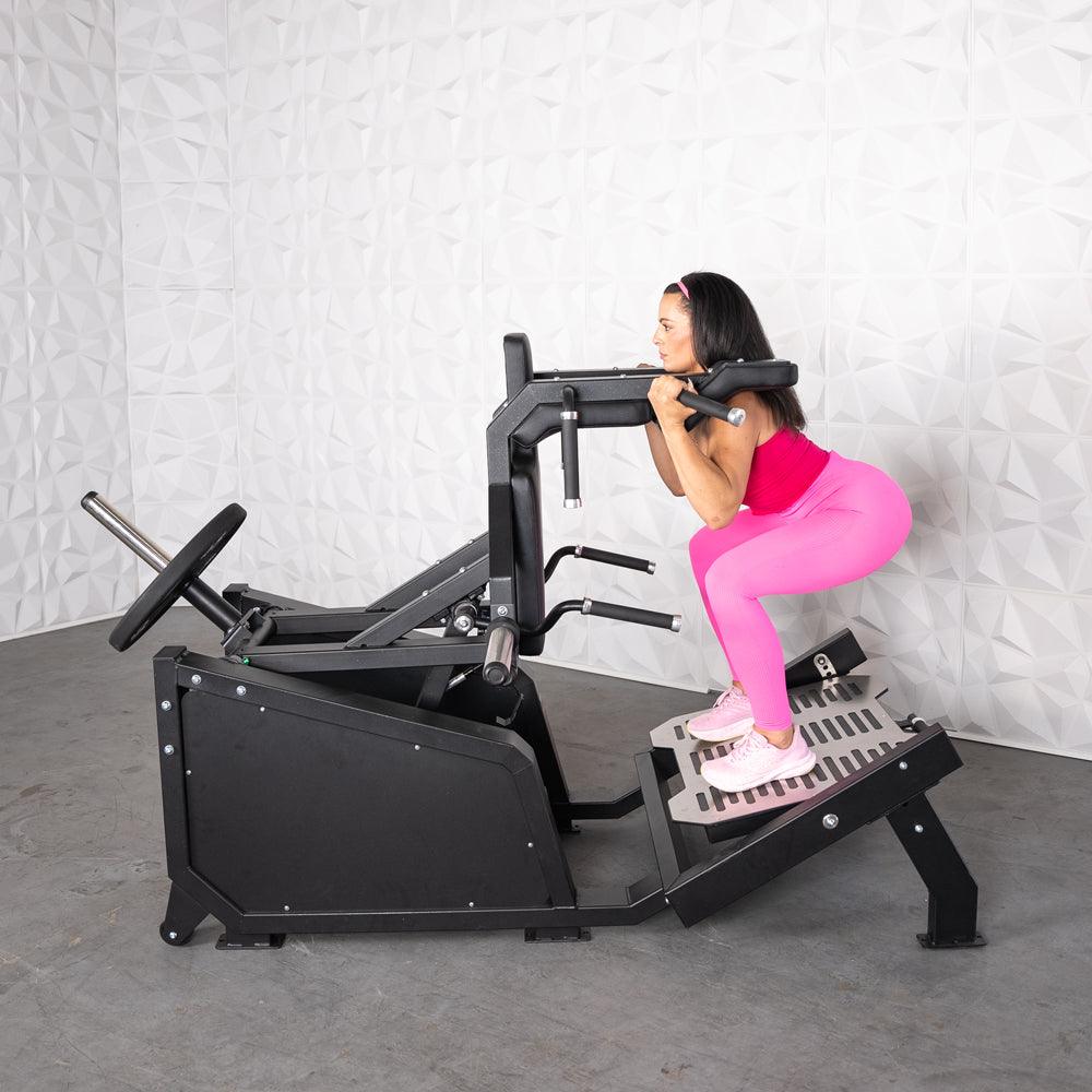 Woman in pink performing a squat on a black plate-loaded hack squat machine.
