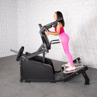 Thumbnail for Woman in pink using a black plate-loaded hack squat machine.