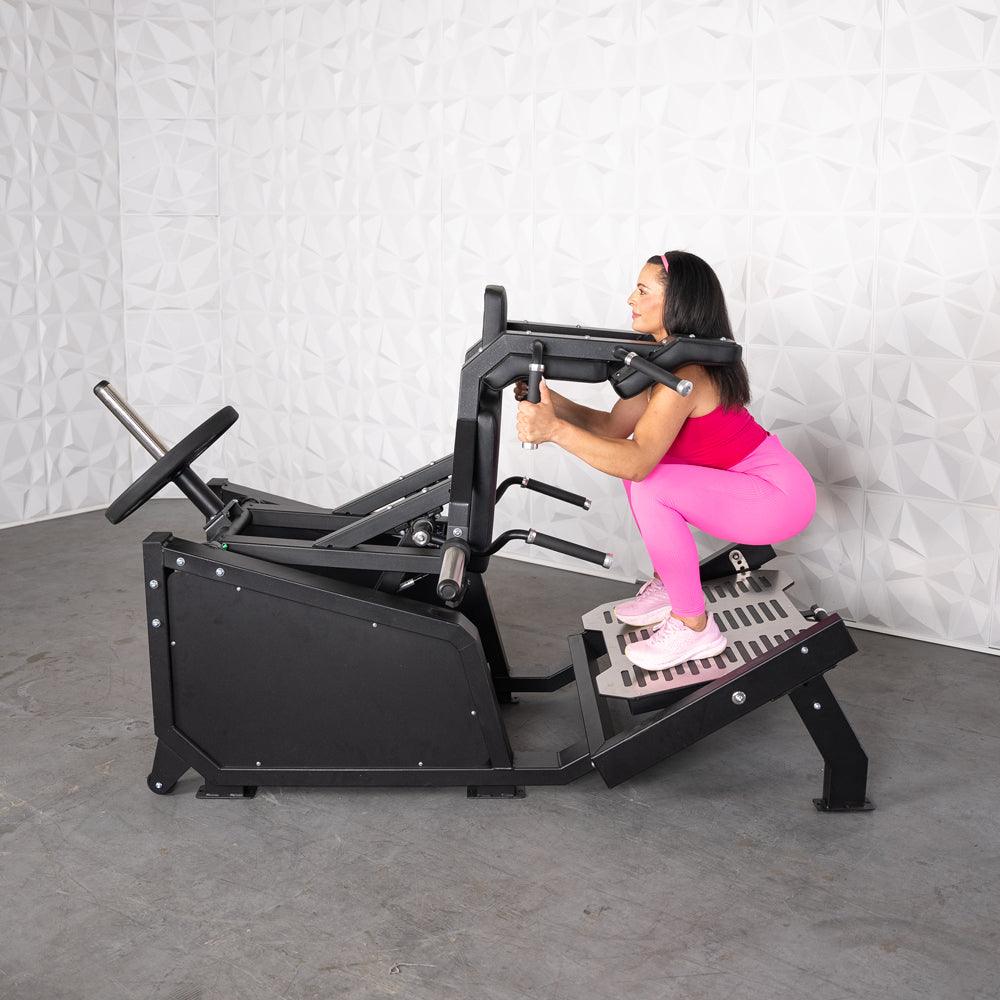 Woman in pink squatting on a black plate-loaded hack squat machine.