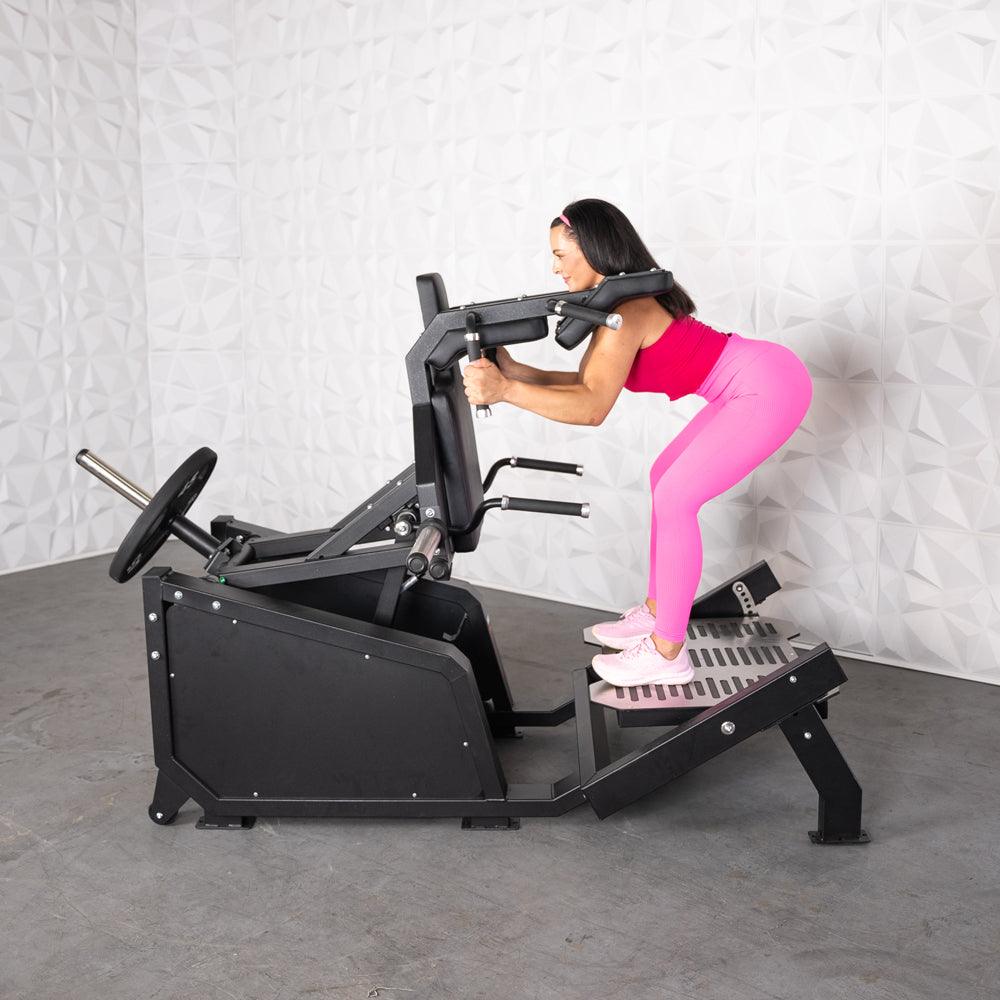 Woman in pink doing a squat on a black plate-loaded squat machine.