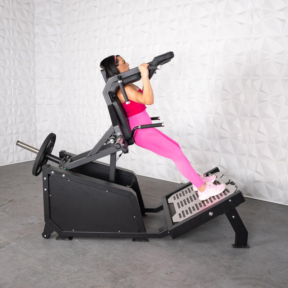Woman in pink using a black plate-loaded hack squat machine.
