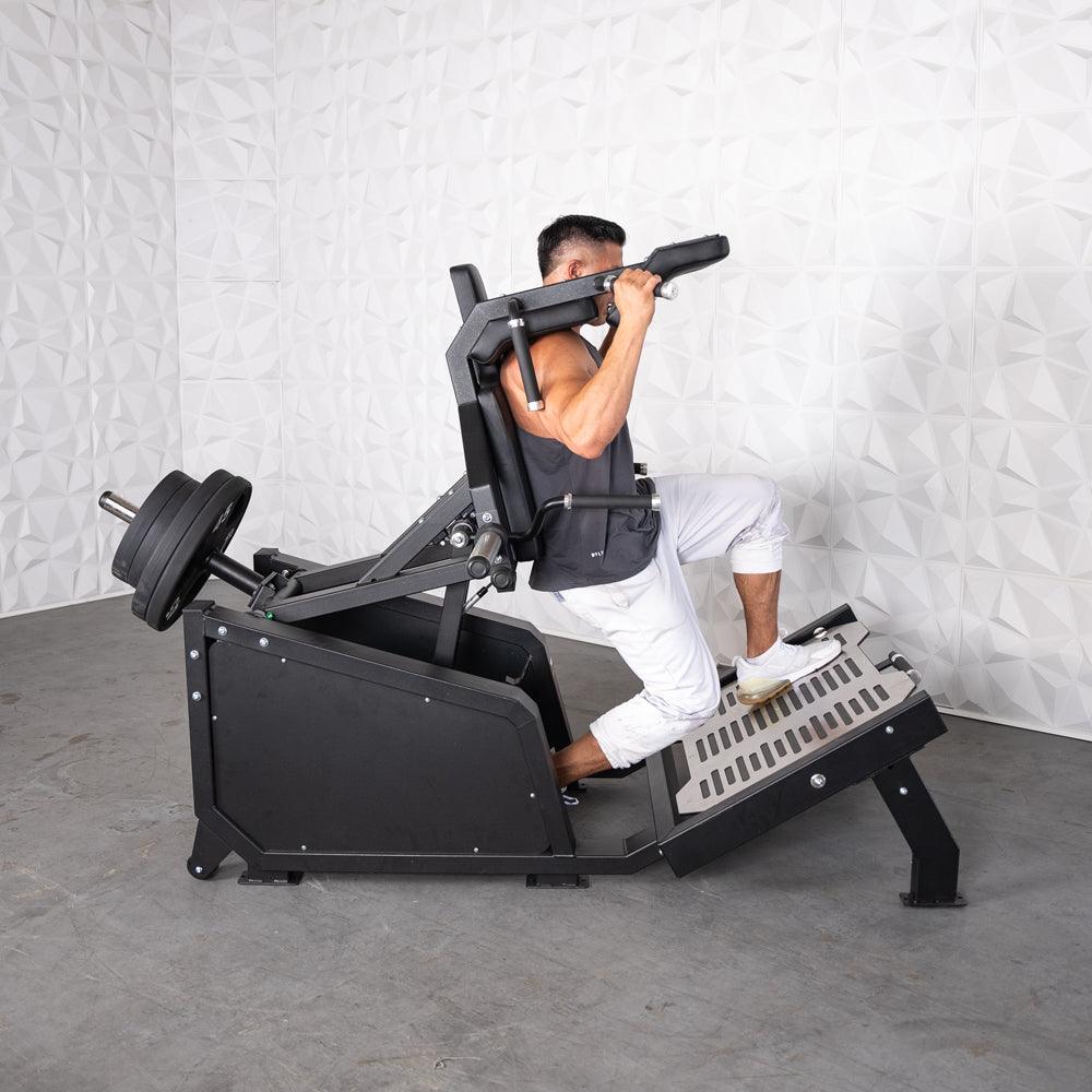 Man using a black plate-loaded hack squat machine with weights on the back.