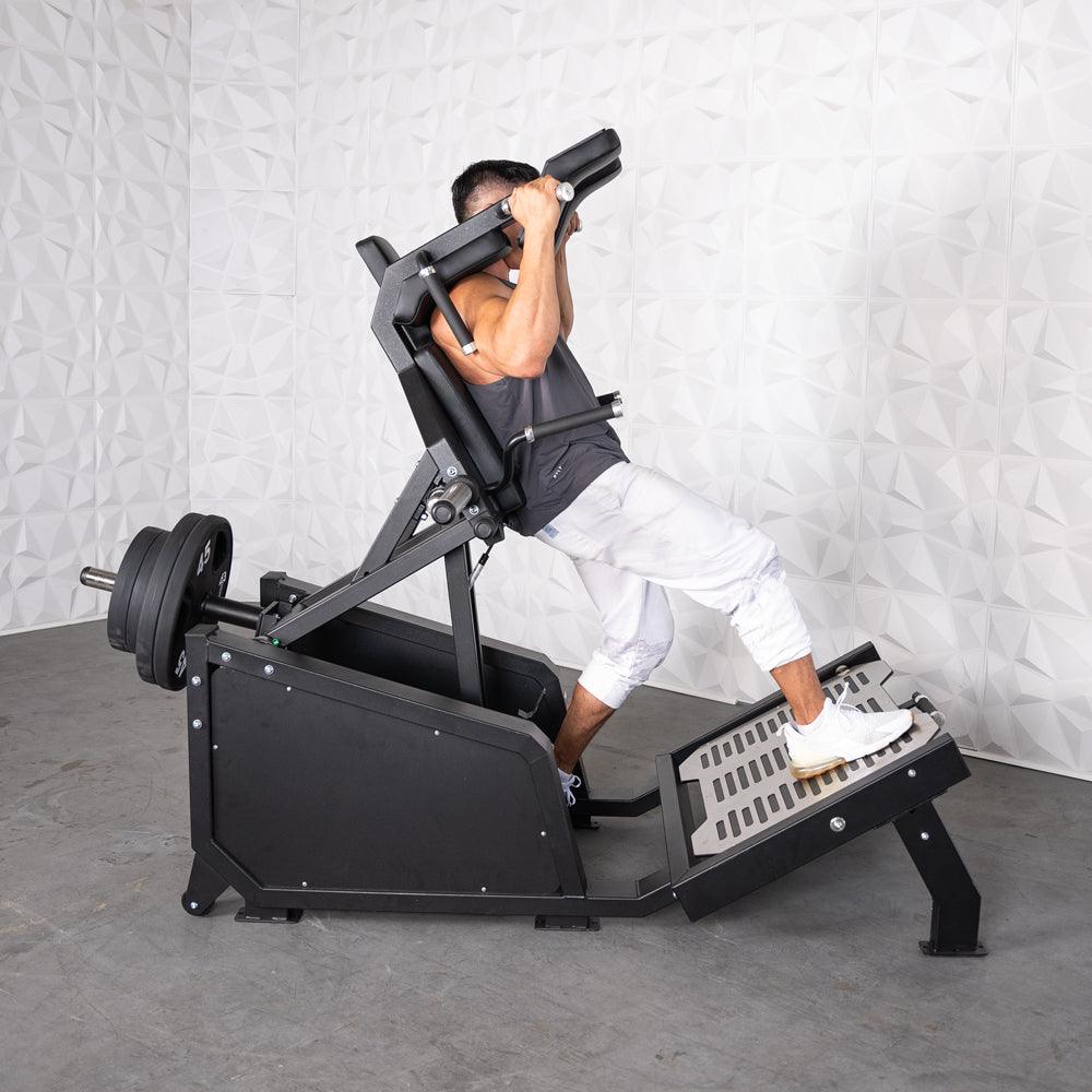 Man using a black plate-loaded squat machine with weights, performing a front squat.