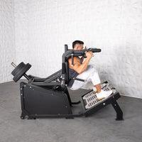 Thumbnail for Man using a black plate-loaded hack squat machine with weights on the back and a textured white wall behind.