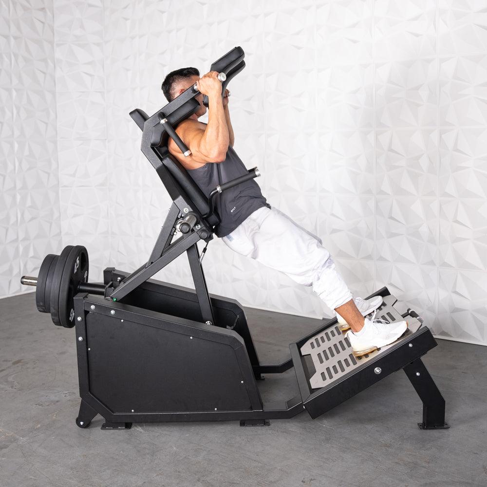 Man performing a hack squat on a black plate-loaded machine with weights.