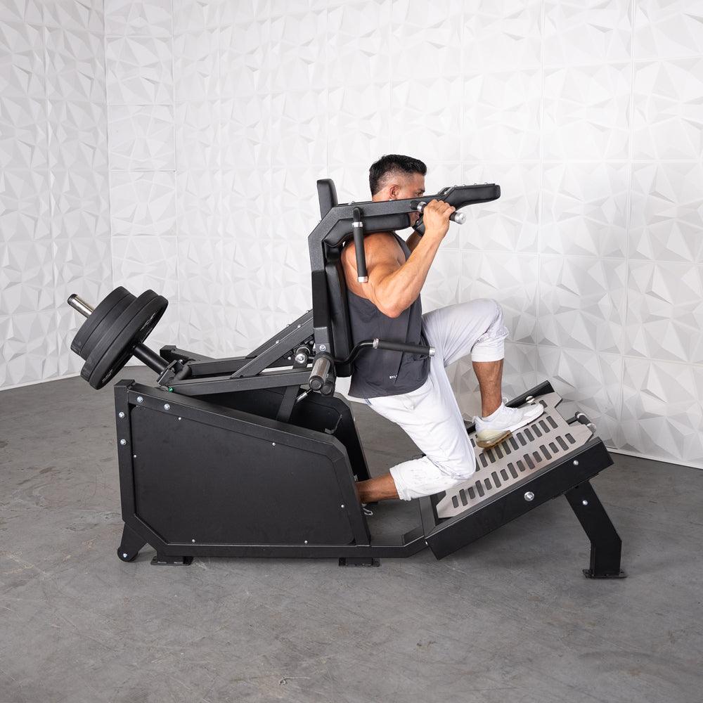Man using a black plate-loaded hack squat machine with weight plates on the back.