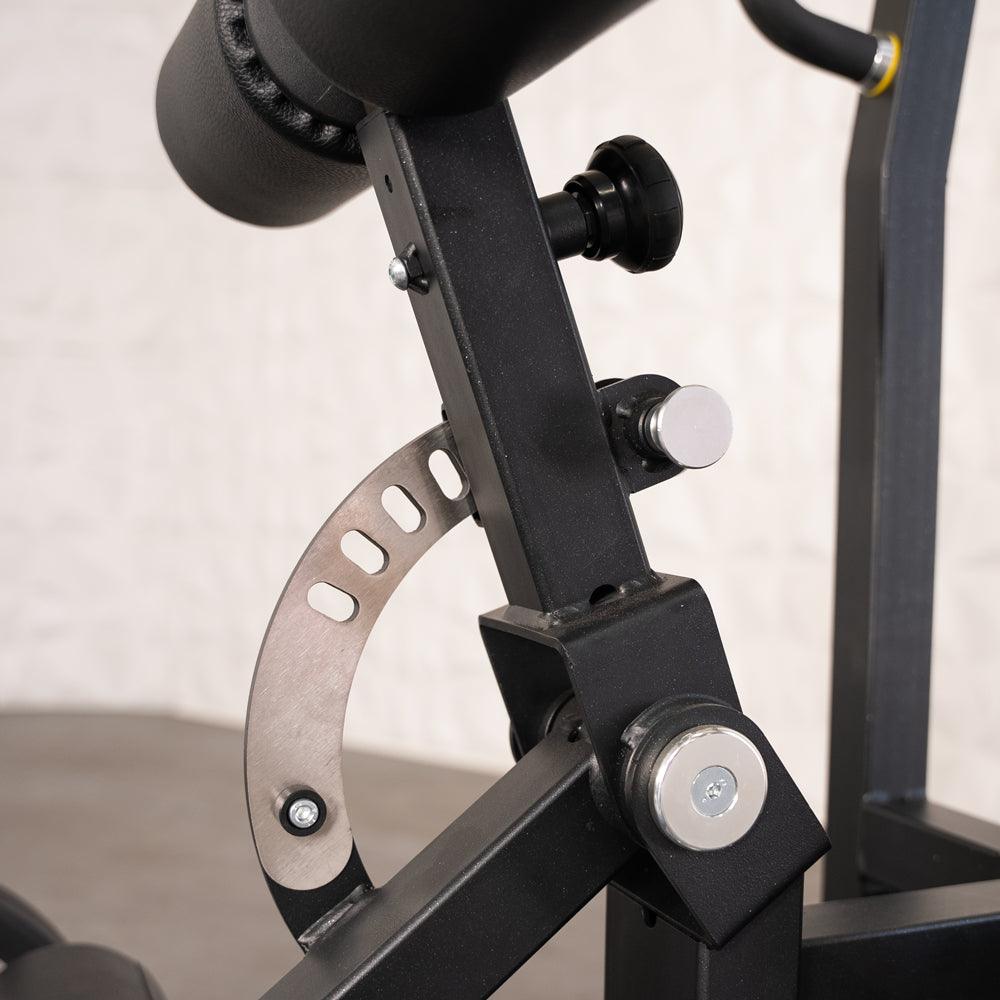 Close-up of the adjustable pad mechanism on a black fitness machine, showing a curved metal plate with holes.