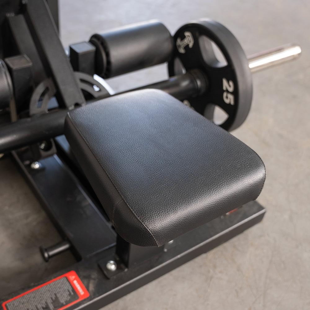 Close-up of the black padded seat and leg roller on a hip thrust machine with a 25lb weight plate.