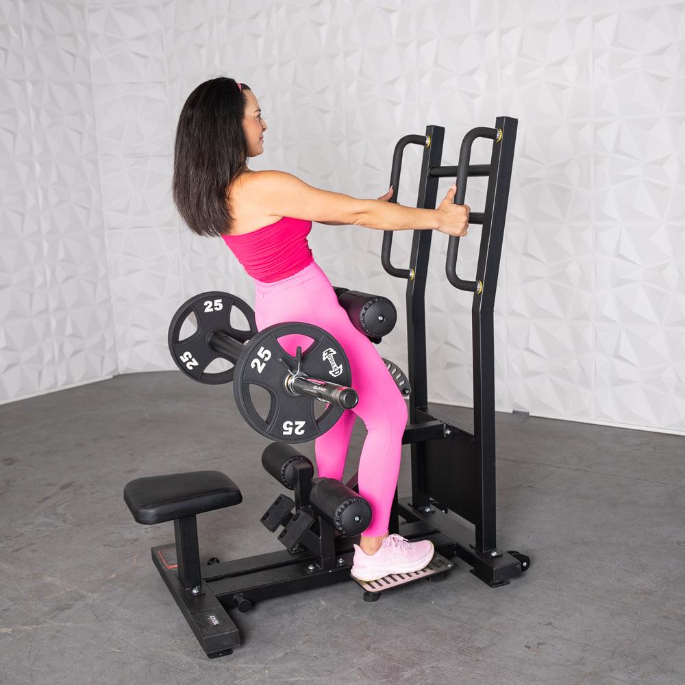 Woman in pink using a black standing hip thrust machine with plate weights.