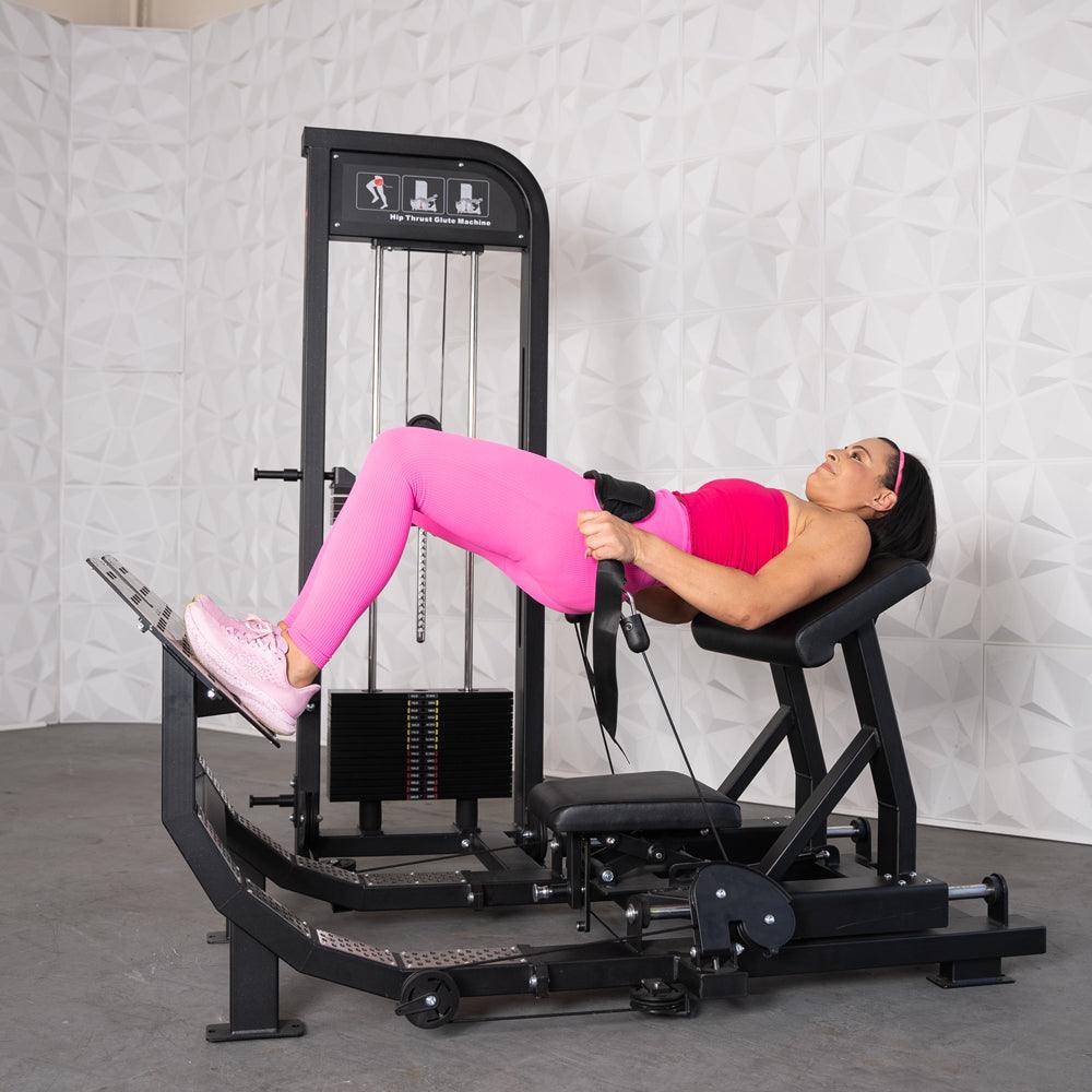 Woman in pink activewear performing a hip thrust exercise on a black selectorized glute drive machine.