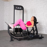 Thumbnail for Woman in pink using a black hip thrust glute machine with weight stack.