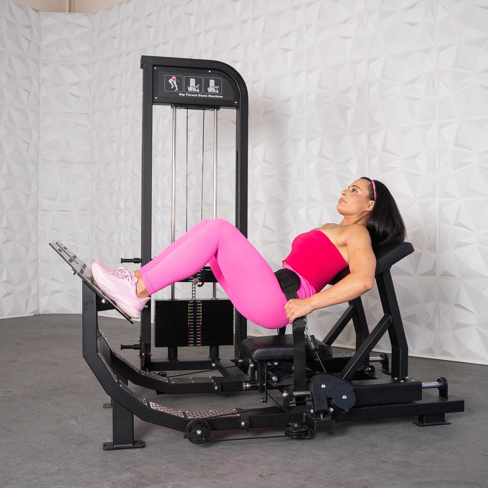 Woman in pink workout gear using a black selectorized hip thrust glute machine.