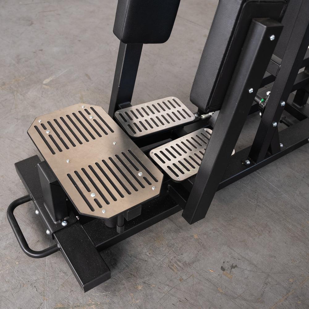 Close-up of the footplates and lower frame of a black and silver standing hip abductor machine.