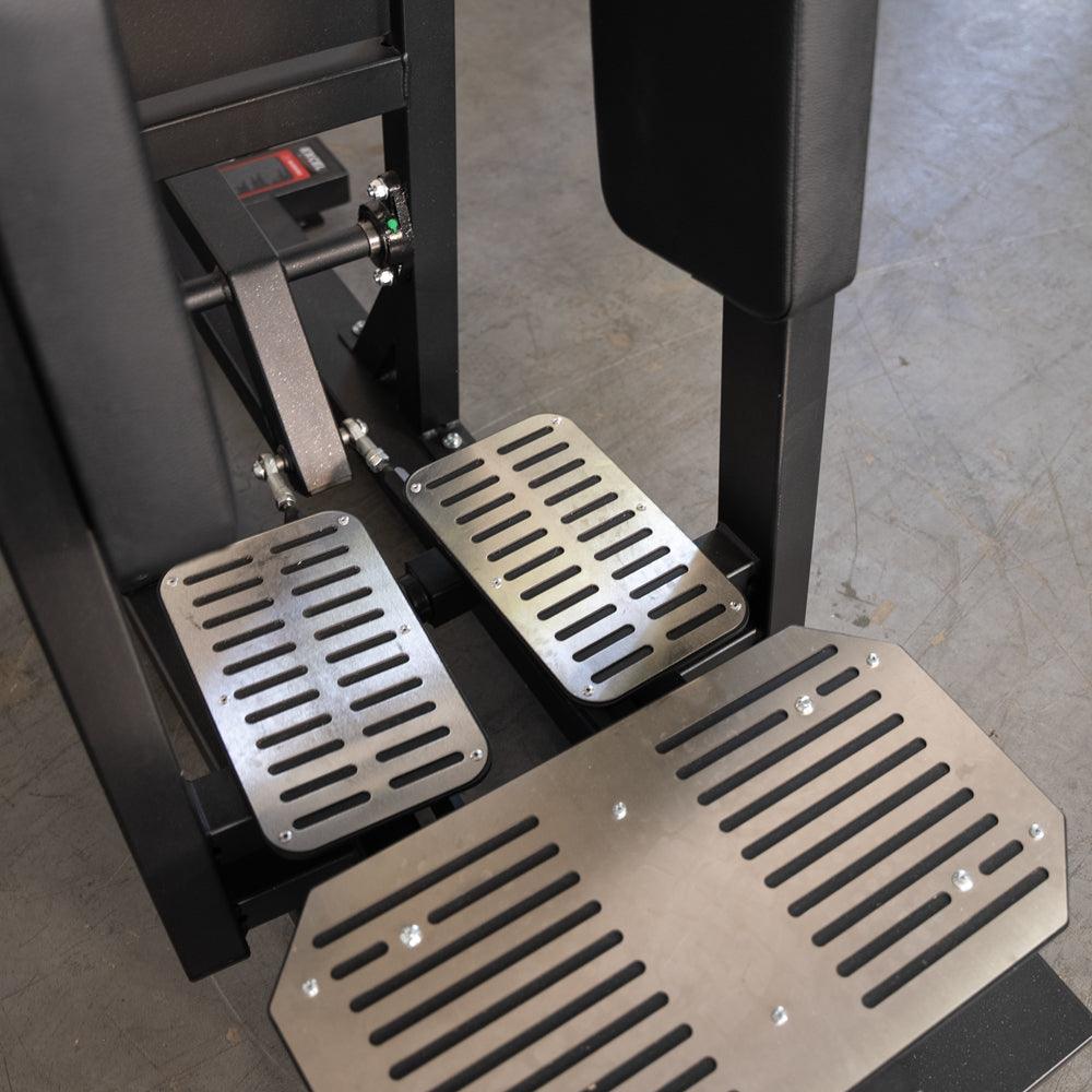 Close-up of a standing hip abductor machine's footplates and lower mechanism.